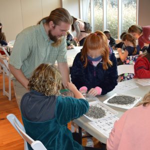 Kids trying to find fossils within their tray with the help of instructor during Fossil Lab