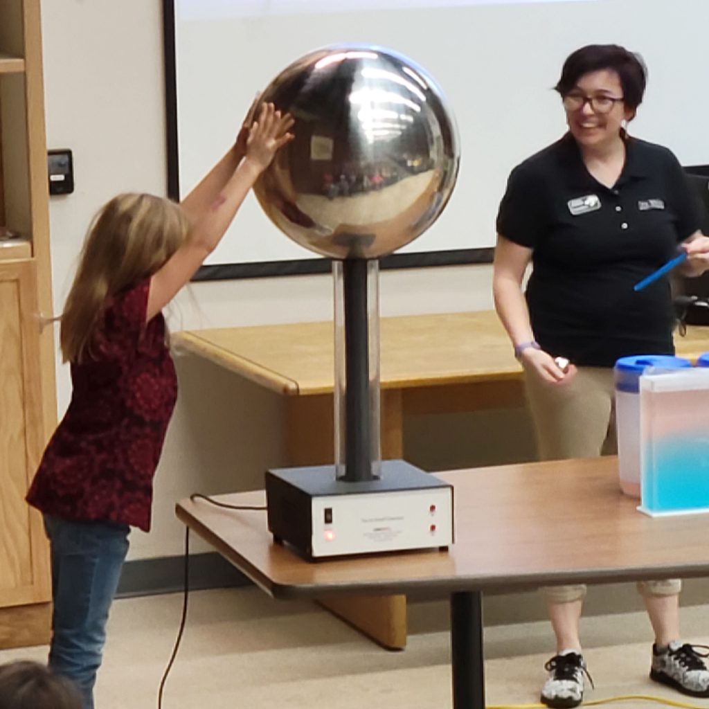 A girl holding placing both of her hands on the Van De Graaff Generator