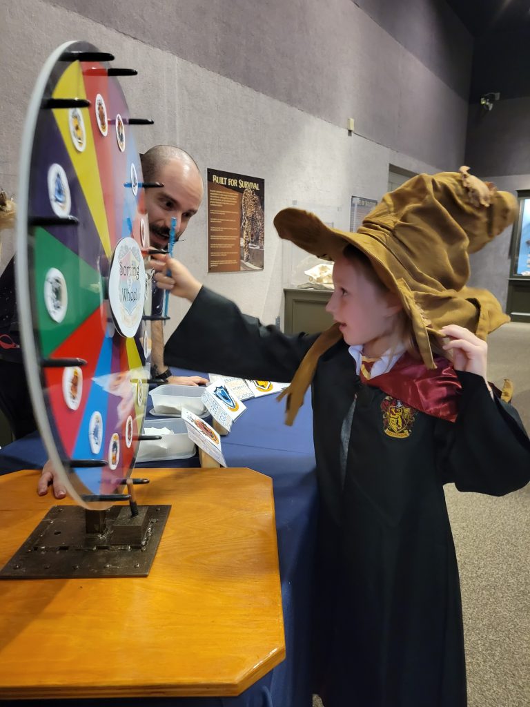 Photograph of a kid in a costume spinning the wheel wearing Harry Potter costume with a sorting hat.