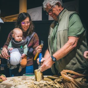 volunteer holding a rock so a mother and her small child can use a hammer to split it