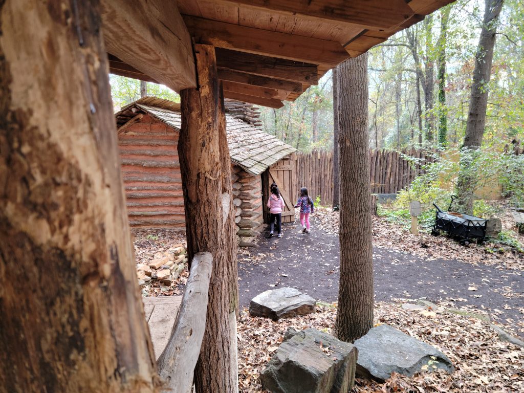 Three children wearing pink exploring the 18th Century log house in the Catawba Village.