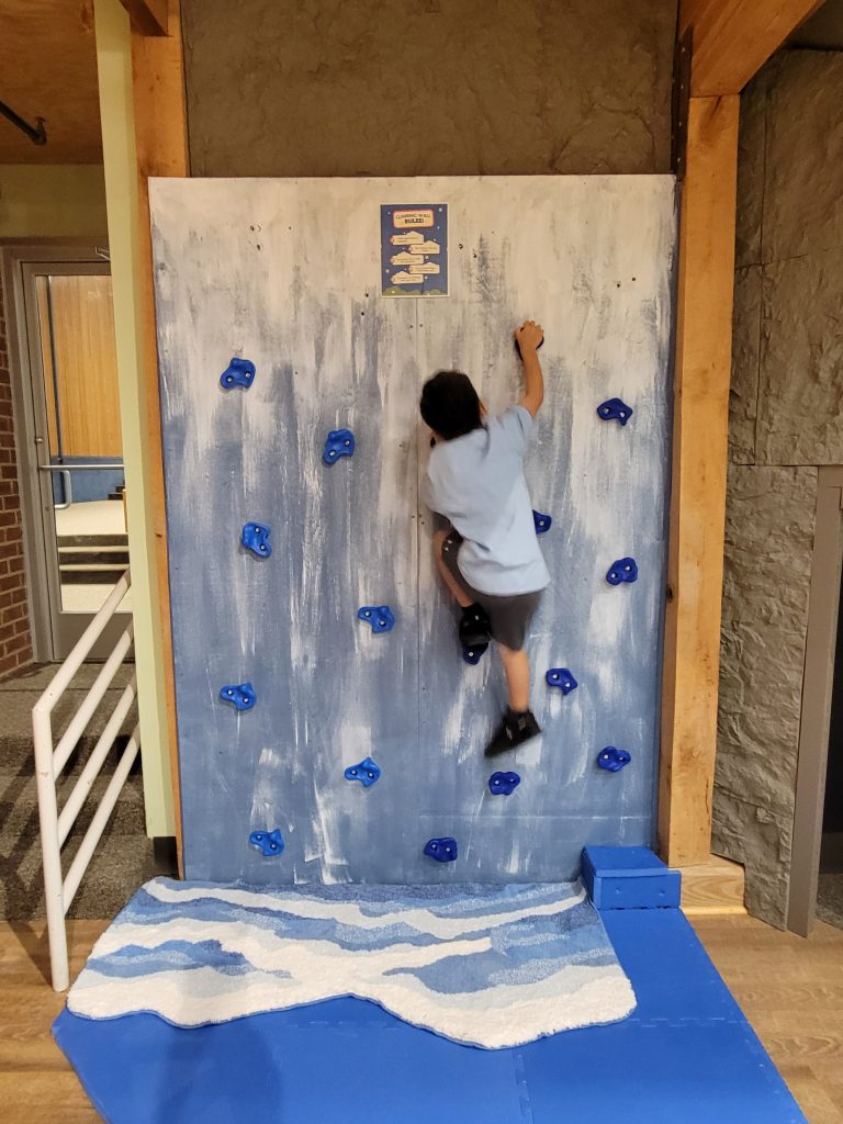 small child climbing rock wall in museum with blue handholds