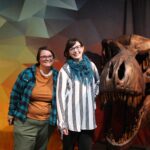 Two women pose with large T. rex skull