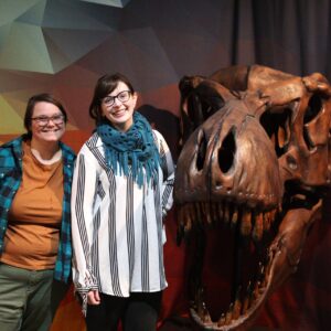 Two women pose with large T. rex skull